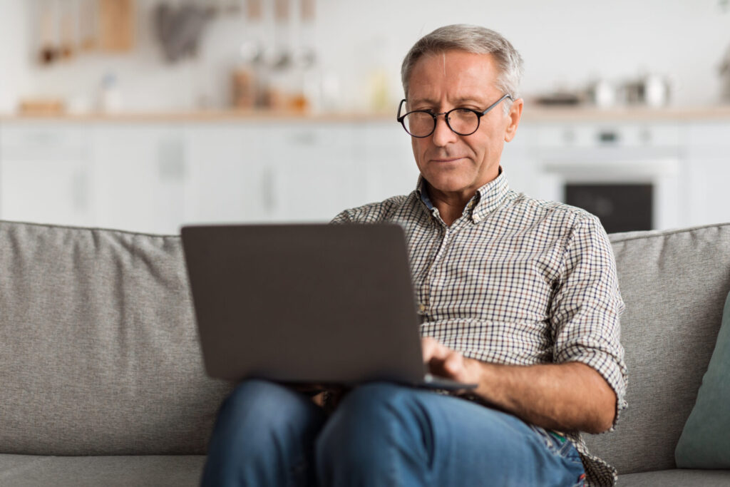 senior male using laptop sitting on couch at home
