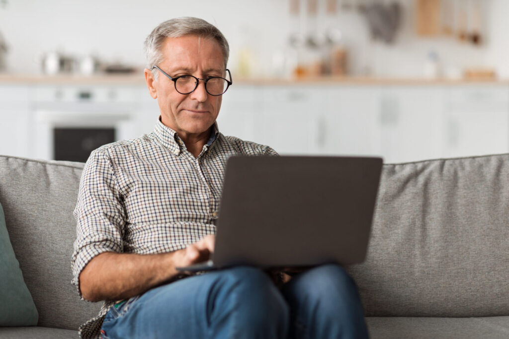 senior male using laptop sitting on couch at home